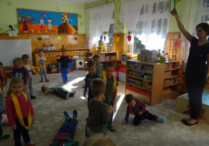 Dzieci w kolorowych szarfach stoją na dywanie
