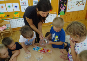 Dzieci z panią mieszają kolorowe kostki lodu z wodą