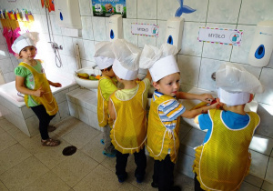 Dzieci w fartuszkach i czapkach kucharzy myją owoce