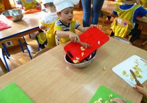 Dzieci przekładają z deseczki do miski pokrojone owoce