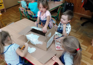 Dzieci zamalowują farbami karton