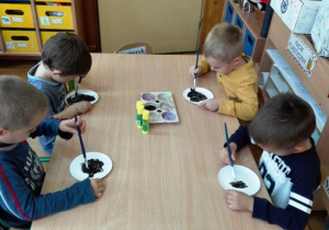 Chłopcy malują czarną farbą papierowe talerzyki