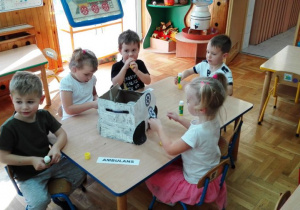Dzieci przyklejają do pomalowanego pudełka napisy