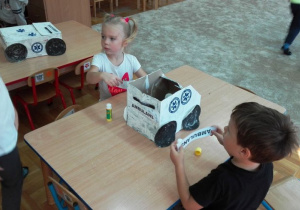 Dzieci przyklejają napisy na autko z kartonu