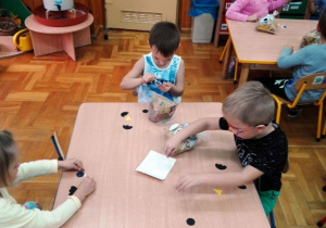 Dzieci przyklejają elementy do woreczka z liścmi