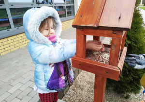 Oliwia wrzuca słonecznik do karmnika.