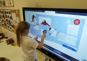 Zuzia układa puzzle przedstawiające sport zimowy na monitorze multimedialnym.
