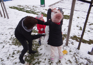 Oliwia, Laura i Szymon lepią przy pomocy pani Reni bałwana.