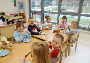 Żabki siedzą przy stolikach i zajadają się ciastem marchewkowym.