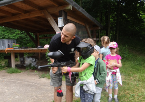 Lenka przy pomocy instruktora strzela z pistoletu do paintballa.