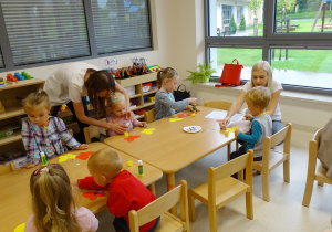 Dzieci przy stolikach wyklejają kolorowymi kółkami motyle.