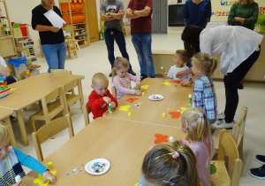 Dzieci przy stolikach kleją na żółtych i czerwonych motylach kolorowe kółka.
