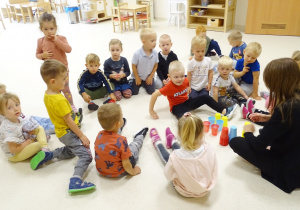 Dzieci wraz z panią siedzą na podłodze. Sebastianek również ułożył kolorowe kubki według kodu.