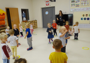 Dzieci oraz pani Ola stoją w rozsypce na kolorowych obręczach tańcząc do piosenki..