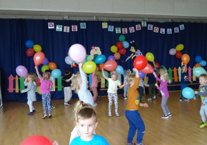 Dzieci tańczą i podskakują trzymając kolorowe balony nad głową.