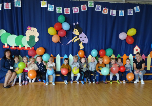 3-4-latki z paniami siedzą na ławce i pozują do grupowego zdjęcia trzymając w rękach balony.