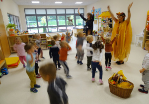 Dzieci i panie tańczą z podniesionymi rękami do piosenki.