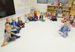 Dzieci siedzą w półkolu na podłodze.