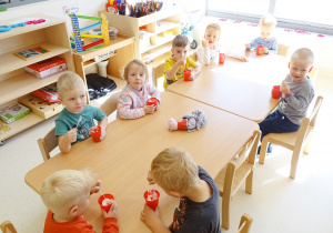 Dzieci siedzą przy stolikach i jedzą galaretki.