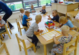 Dzieci siedzą przy stolikach i ozdabiają swoje motyle.