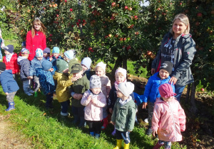 Maluszki razem z paniami pozują do zdjęcia grupowego na tle jabłoni.