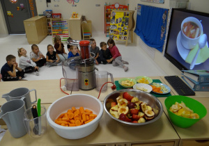 Dzieci oglądają filmik, w tle przygotowane składniki na sok
