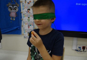 Chłopiec z zawiązanymi oczami trzyma w rączce marchewkę