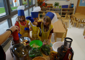 Dziewczynki wkładają owoce i warzywa do sokowirówki