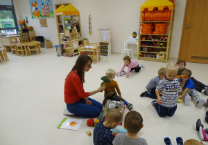 Dzieci siedzą na podłodze. Nauczycielka podaje chłopcu brokuła.