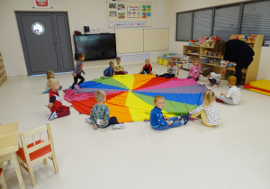 Dzieci siedzą dookoła chusty animacyjnej położonej na podłodze.