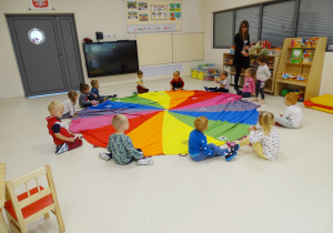 Dzieci siedzą dookoła rozłożonej na podłodze chusty animacyjnej. Umieszczają obrazki zgodnie z kolorem.