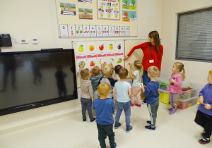 Dzieci dopasowują swoje małe obrazki do obrazków owoców znajdujących się na tablicy. Pani pokazuje obrazek z winogronem.