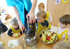 Wiktor wyciska sok z jabłka, pani mu pomaga. Pozostałe dzieci obserwują.