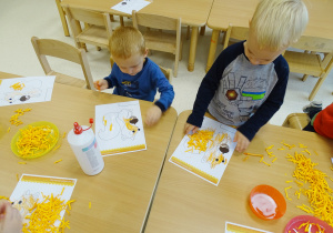 Chłopcy wyklejają przy stoliku ogon wiewiórki za pomocą pomarańczowych ścinków.