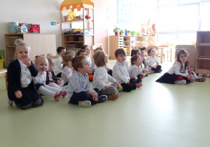 Dzieci siedzą na podłodze i oglądają przedstawienie