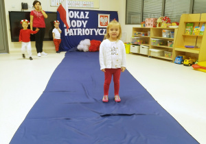 Kinga ubrana na biało czerwono pozuje podczas "Pokazu mody patriotycznej" na granatowym dywanie.