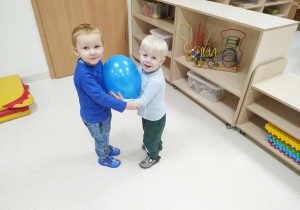 Miłoszek i Juluś bawią się niebieskim balonem, trzymając go między swoimi brzuchami.