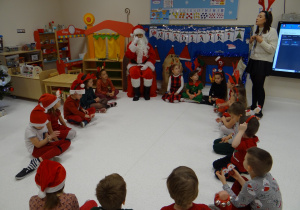 Dzieci siedząc w kole recytują Mikołajowi wiersz po angielsku