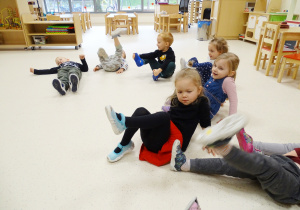 Dzieci siedzą na podłodze i pokazują swoje stopy.