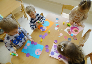 Dzieci wykonują pracę plastyczną przy stolikach, wykorzystując koła.