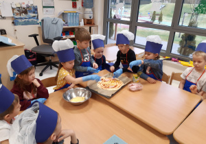 Dzieci w jednorazowych rękawiczkach układają dodatki na pizzę