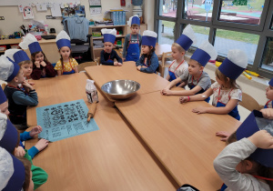 Dzieci siedzą przy stole w czapkach kucharskich