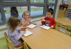 Dzieci siedzą przy stoliku i jedzą pizzę