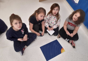 Dzieci w siedzą w małej grupie Oliwia wyjmuje ilustracje planet z koperty