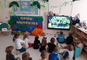 Przedszkolaki oglądają na tablecie film o dinozaurach