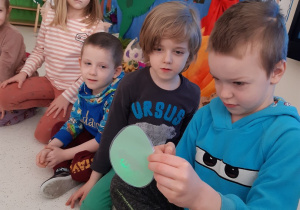 Chłopiec podświetla latarką papierowe jajo z ukrytym w środku dinozaurem