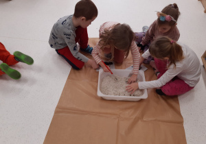 Dzieci szukają kości dinozaura w kuwecie wypełnionej piaskiem kinetycznym