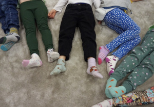 Dzieci z grupy Kotki leżą na dywanie prezentując skarpety nie do pary