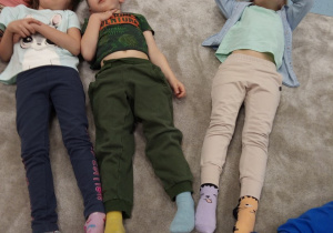Dzieci z grupy Kotki leżą na dywanie prezentując skarpety nie do pary