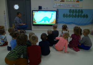 Dzieci oglądają na tablecie film o dinozaurach.